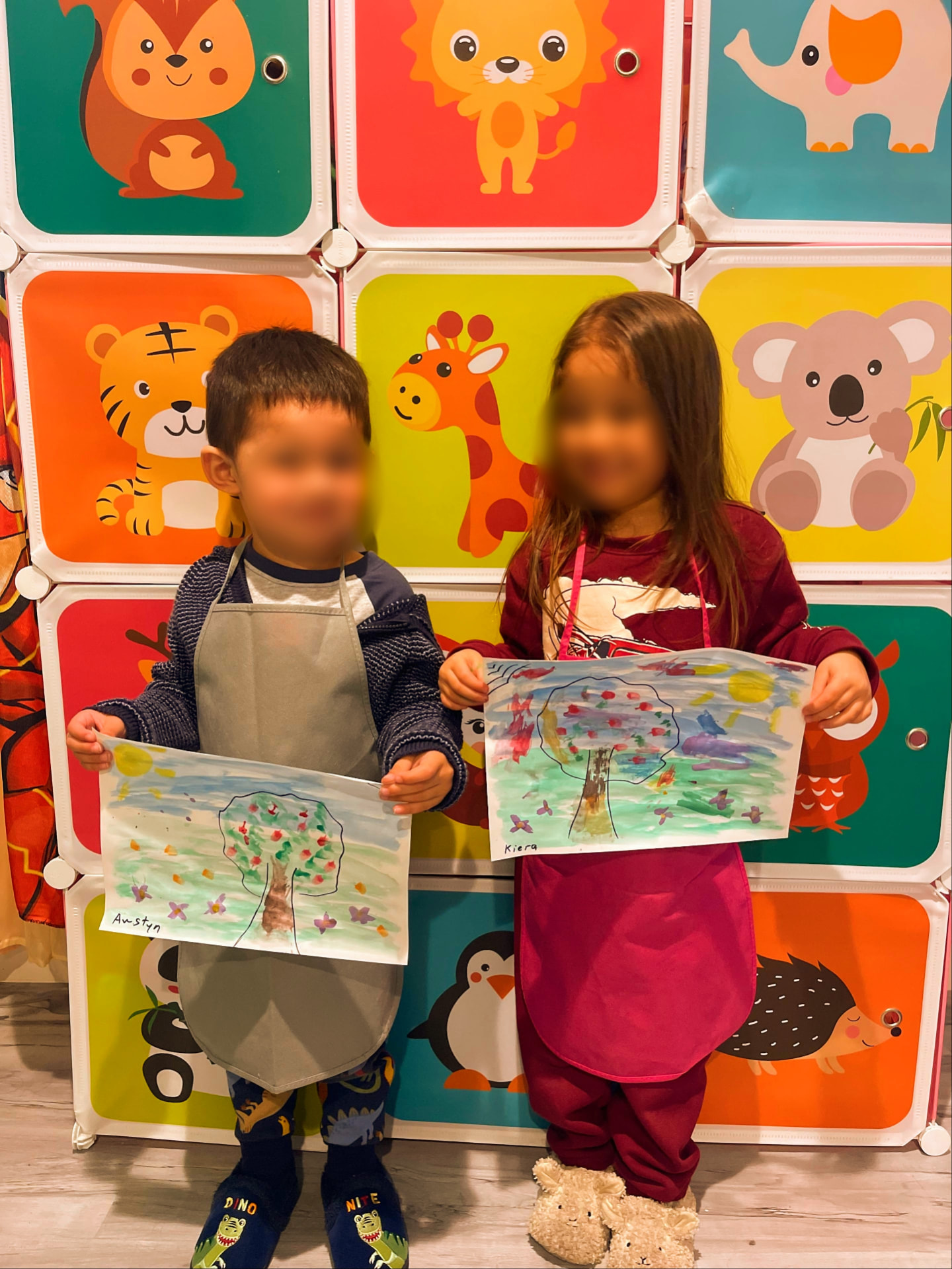 Two children proudly holding up their painted tree artwork