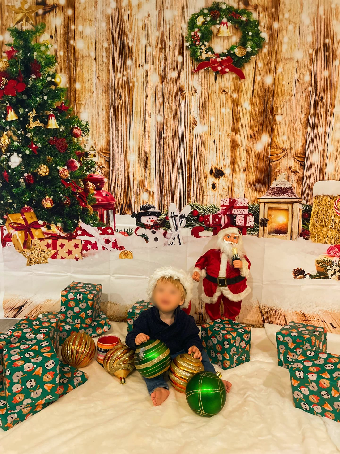Toddler in a Santa hat sitting among ornaments in front of a holiday backdrop