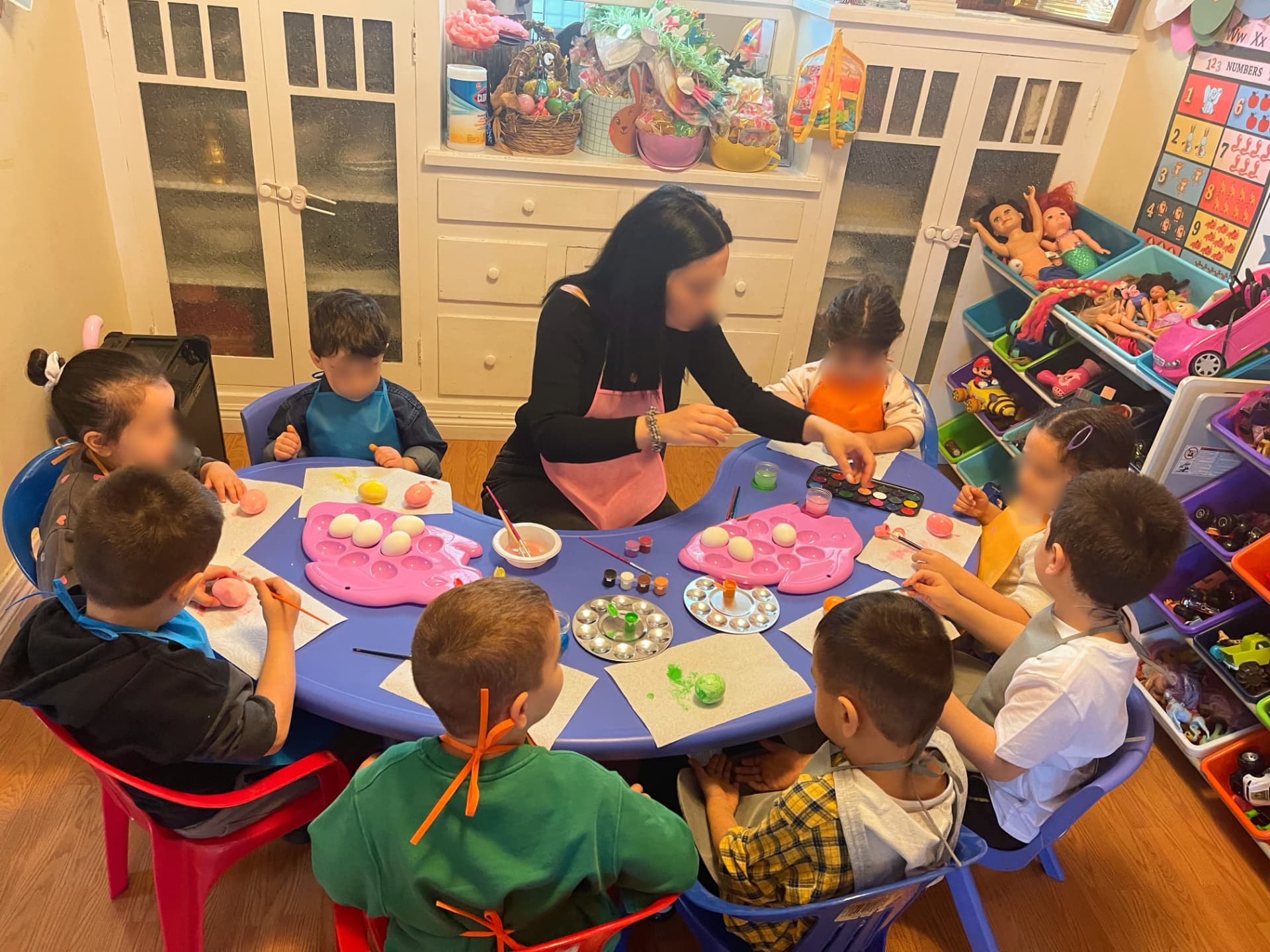 Caregiver and children painting eggs together at an indoor table