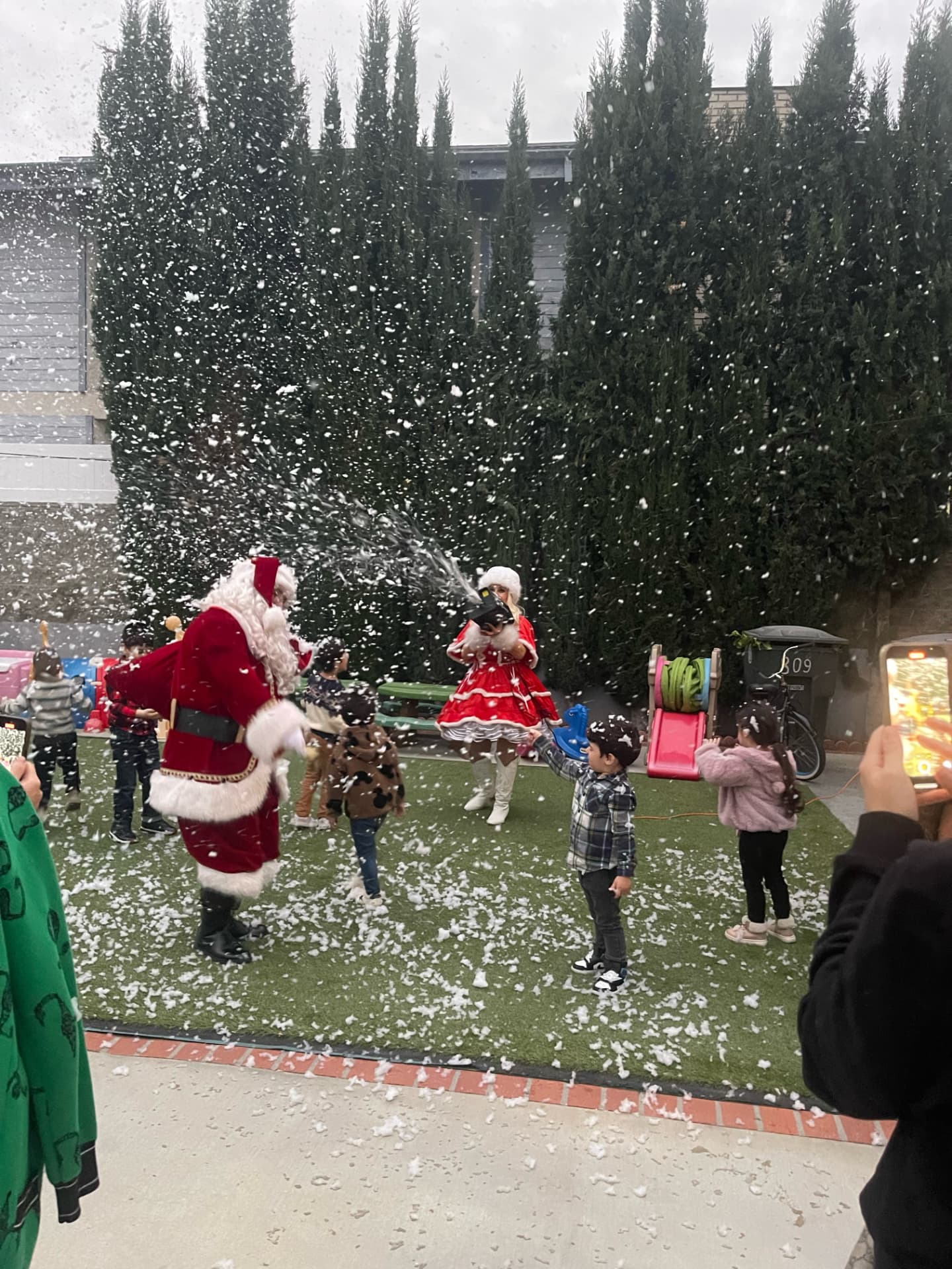 Santa and Mrs. Claus spraying snow over children playing in the backyard