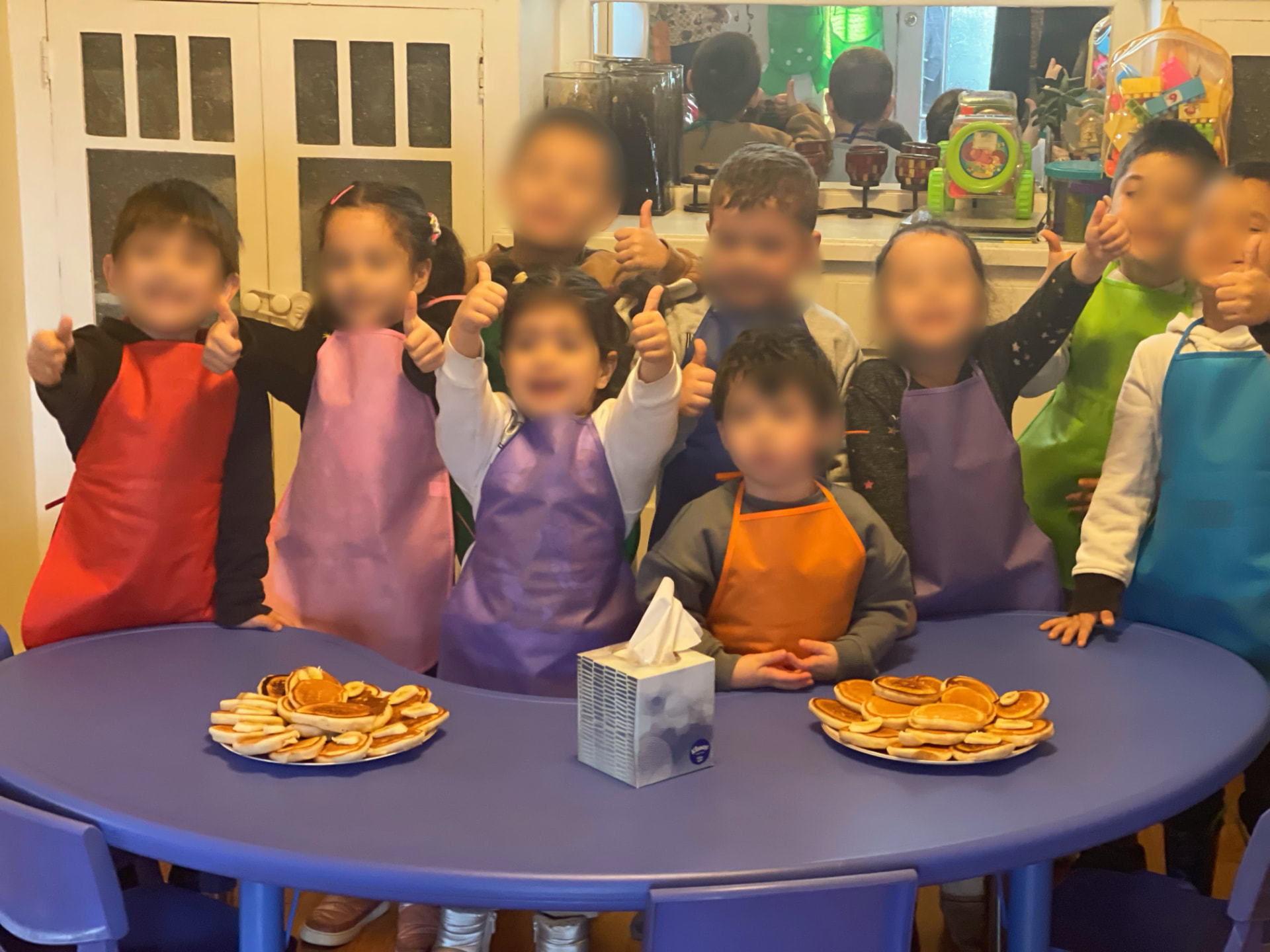 Children in aprons giving thumbs up behind plates of homemade pancakes