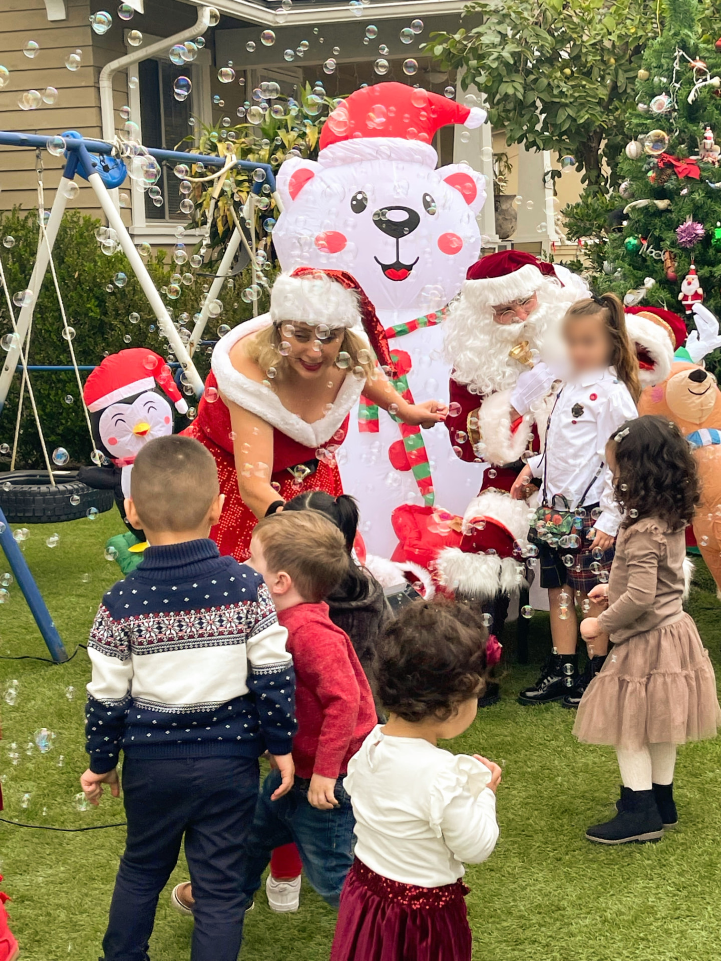 Santa, Mrs. Claus, and a polar bear character greeting children among bubbles in the backyard