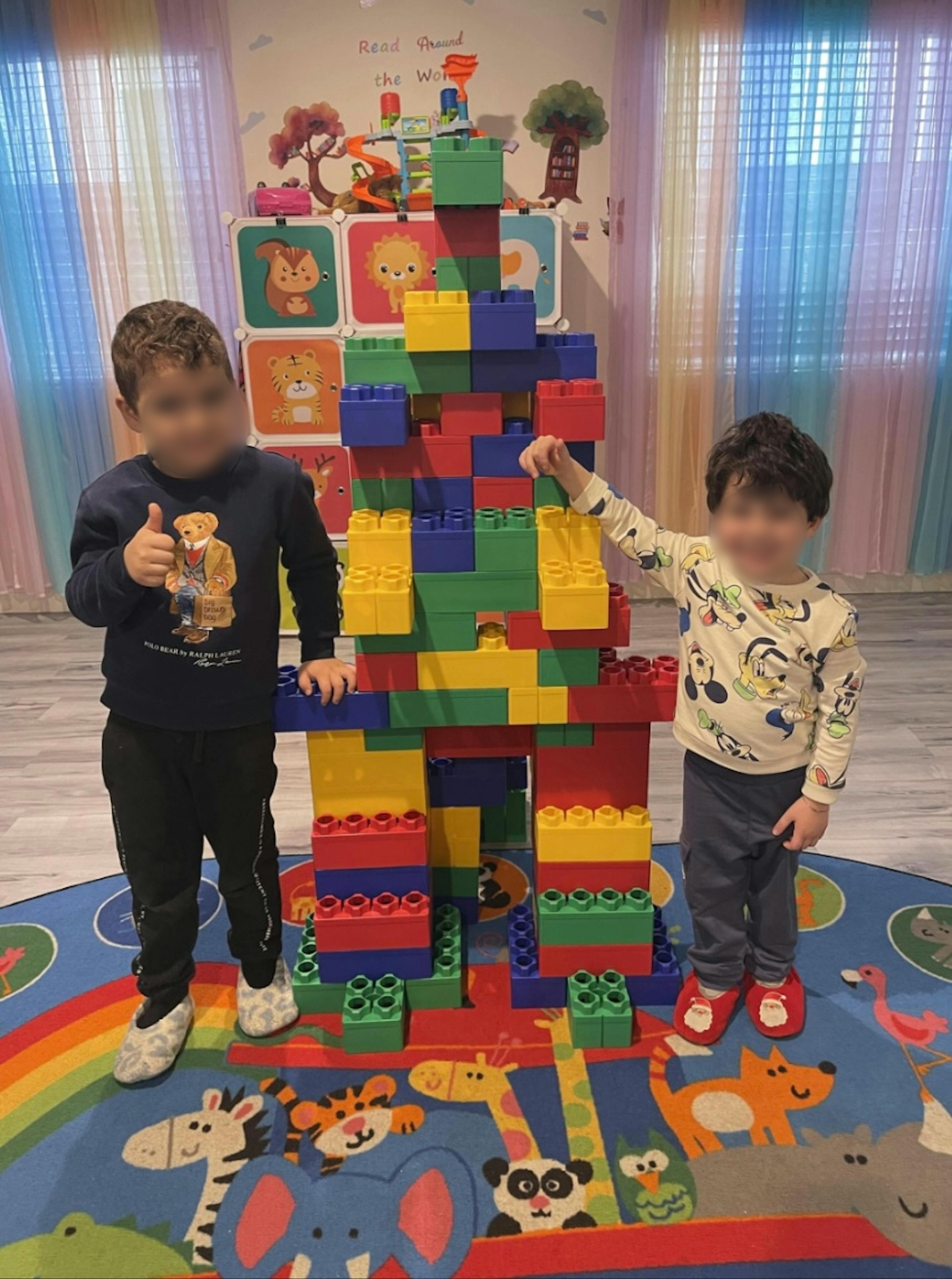 Two children proudly standing next to a tall colorful block tower they built