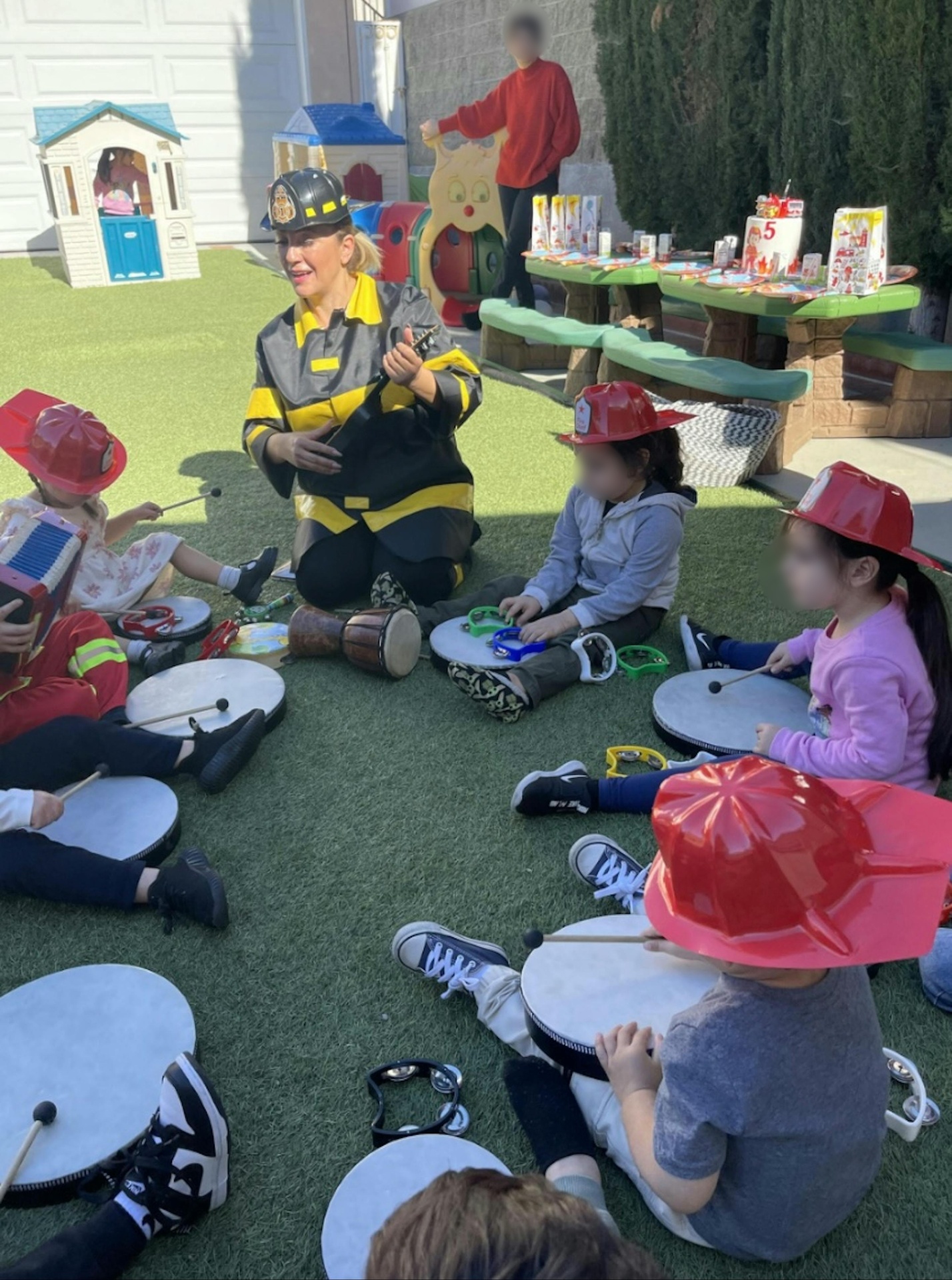 Caregiver in a firefighter costume leading a music circle with children on the grass