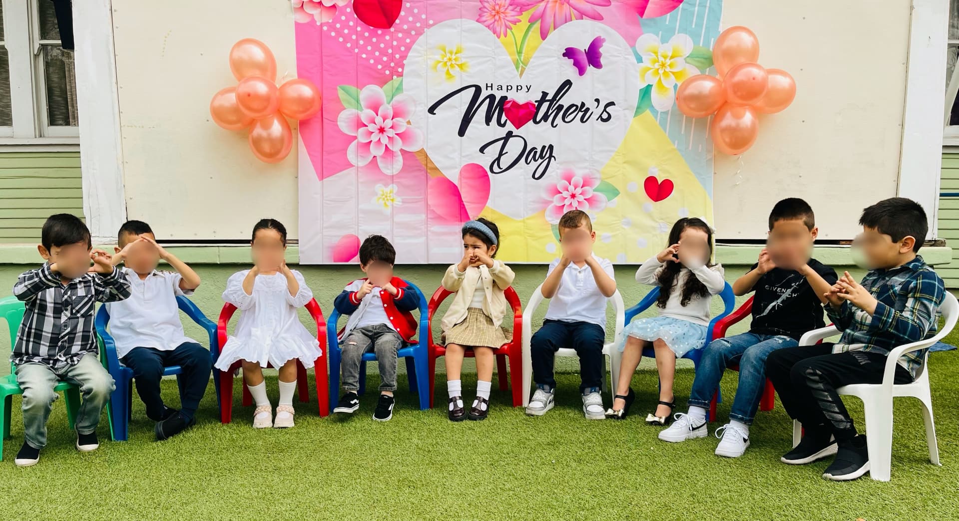 Children seated in a row in front of a Happy Mother's Day backdrop