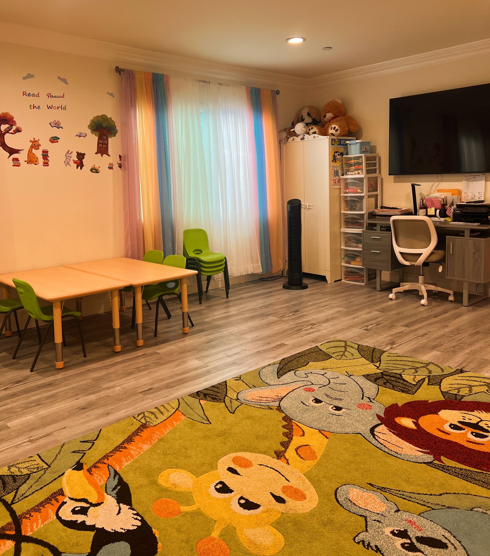Bright activity room with rainbow curtains, learning tables, and a jungle rug