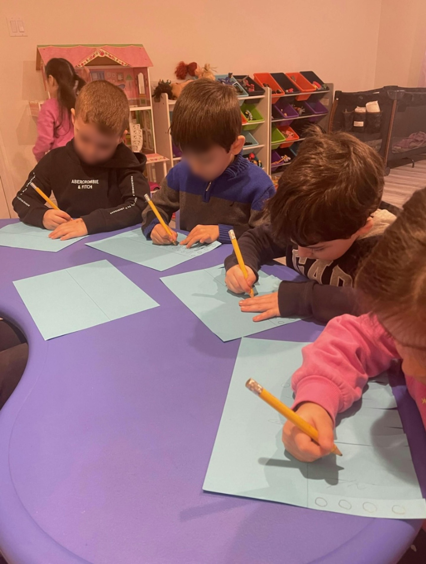Children practicing letters and numbers with pencils at a purple table