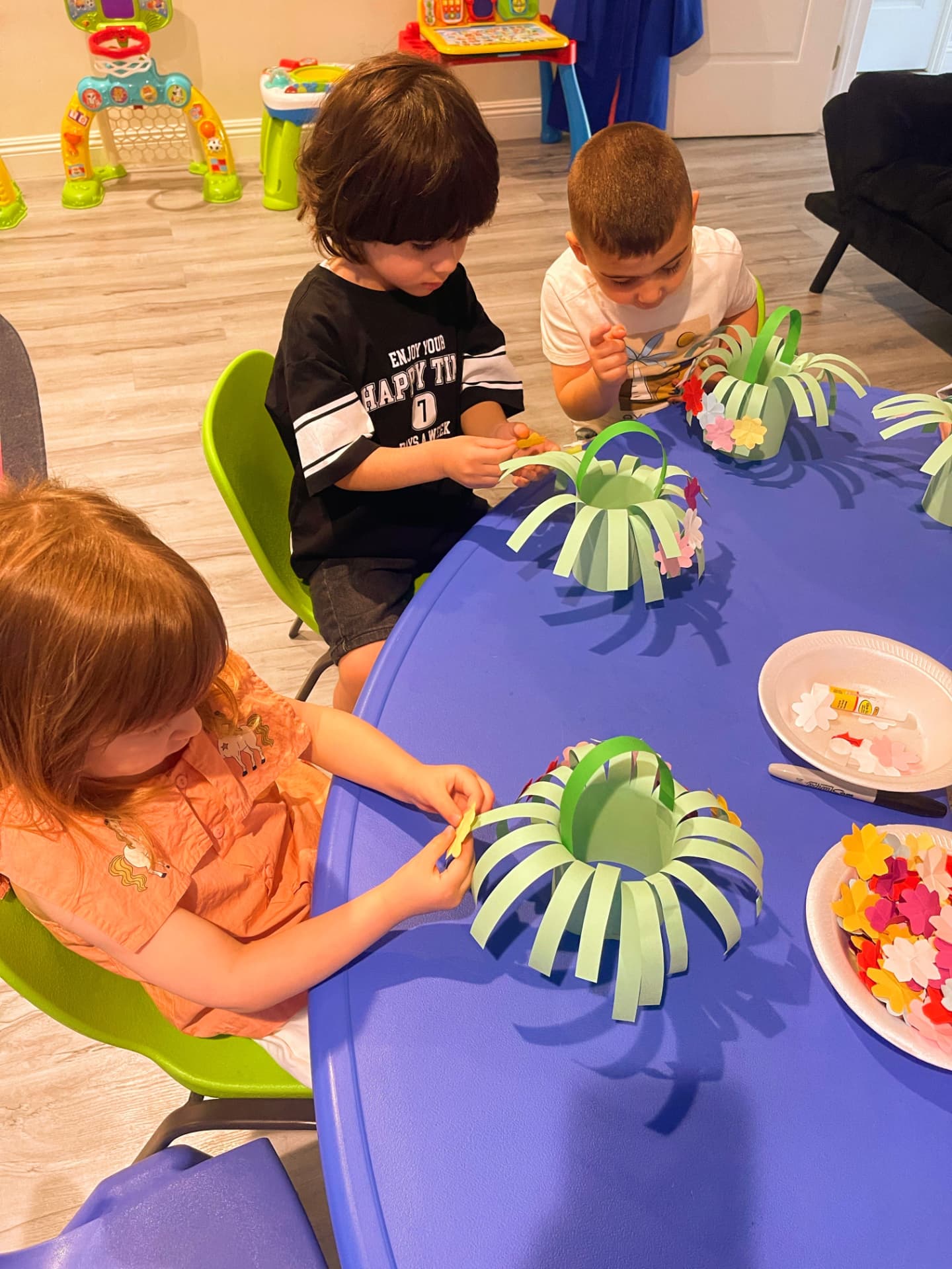 Three children gluing paper flowers onto green paper baskets